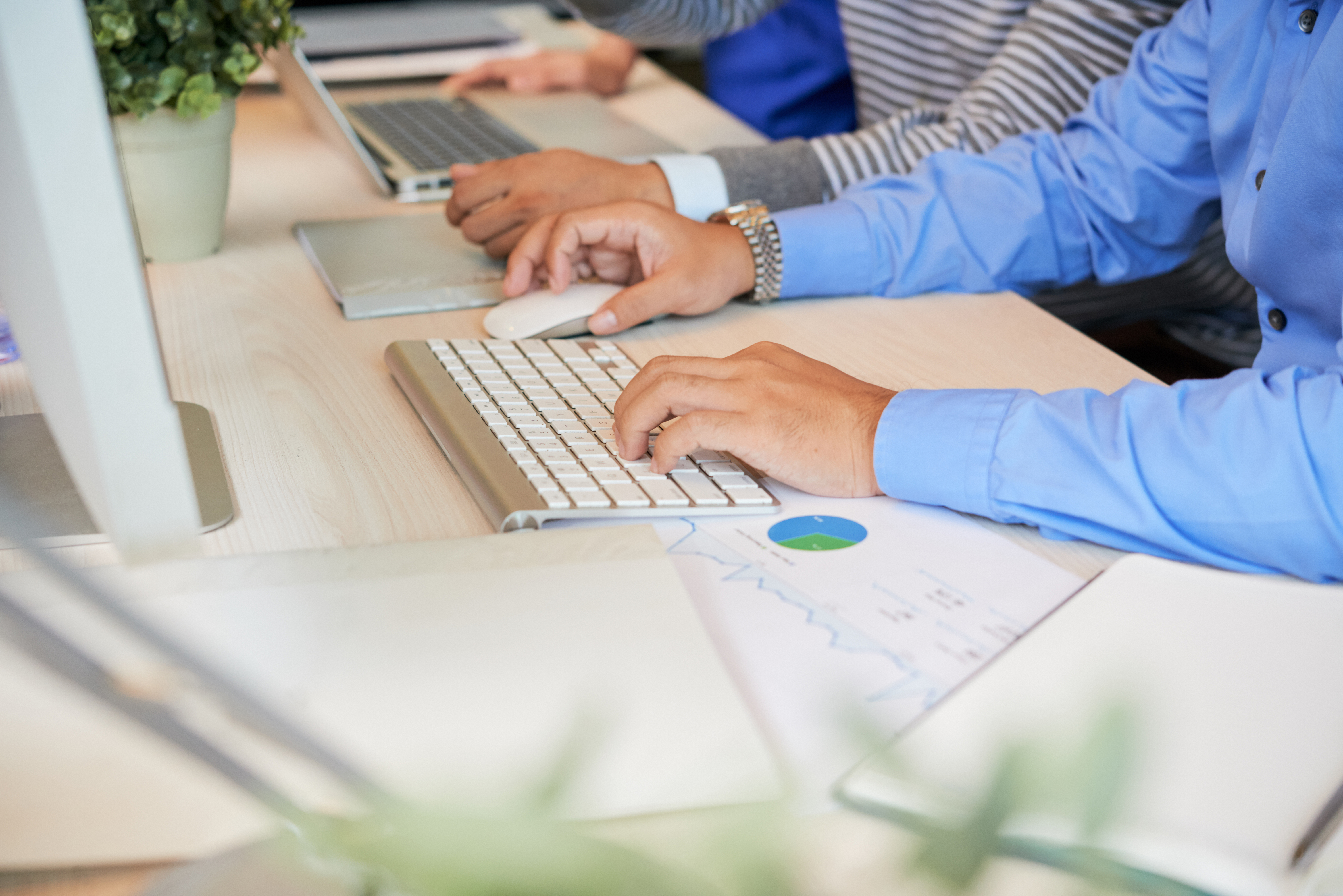 Faceless shot of man sitting with colleagues at table in office and using computer while working