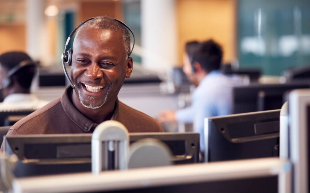 A mature man with a headset on looking at his computer smiles