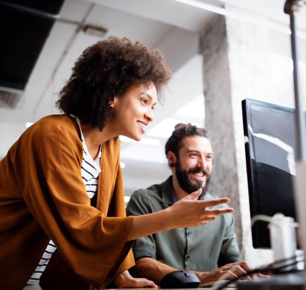 2 professionals in an office setting smile and look at a computer together