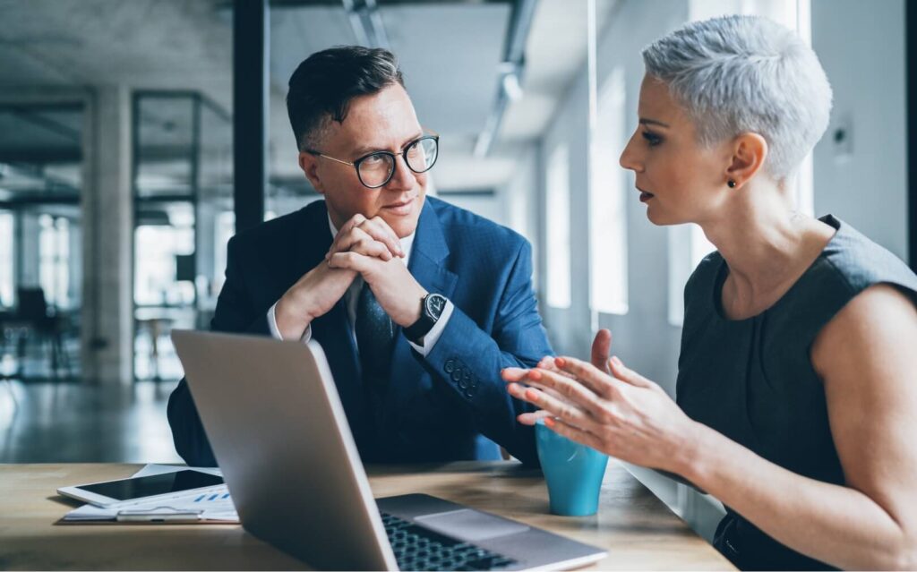 2 professionals, one male and one female talk in an office setting