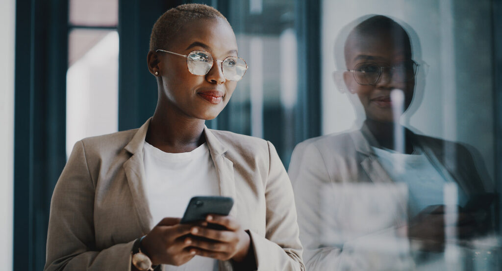 A young, black female professional with short blonde hair looks out of a window while holding a cellphone