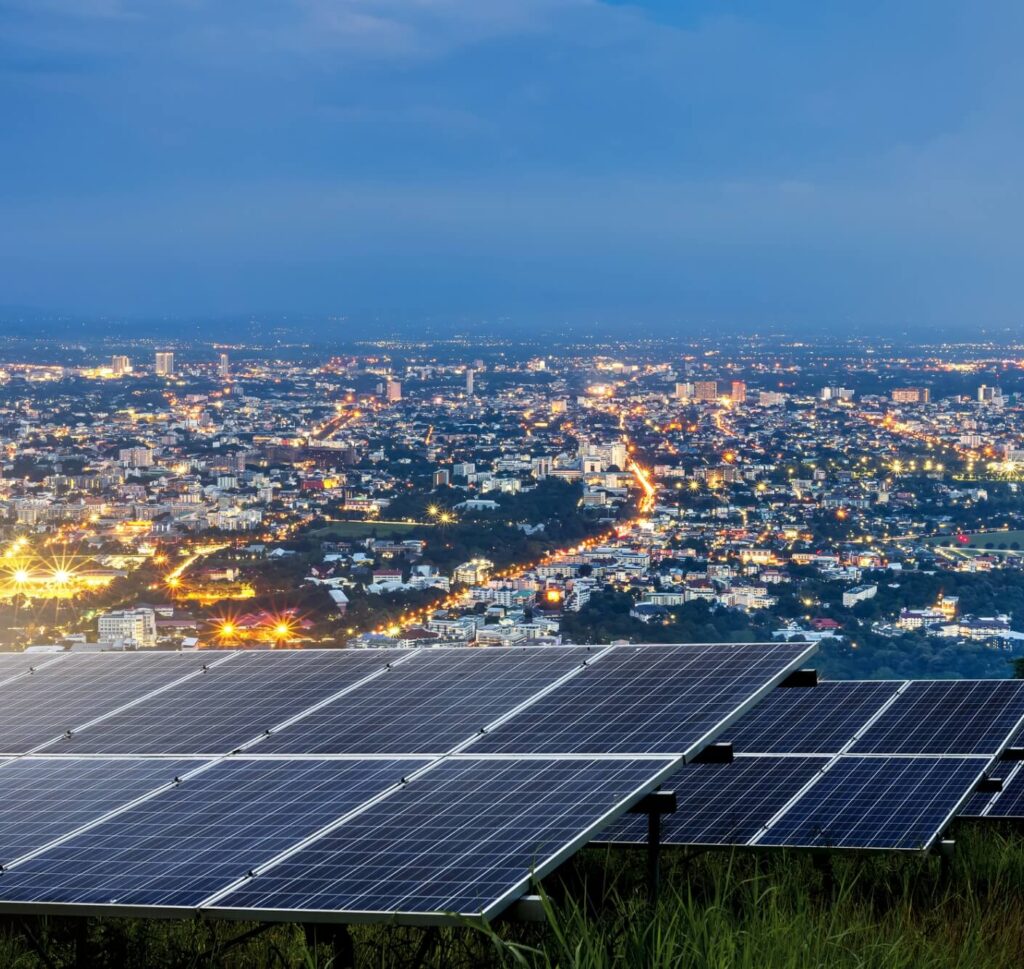 An array of solar panels in the foreground with a city lit up at night in the background