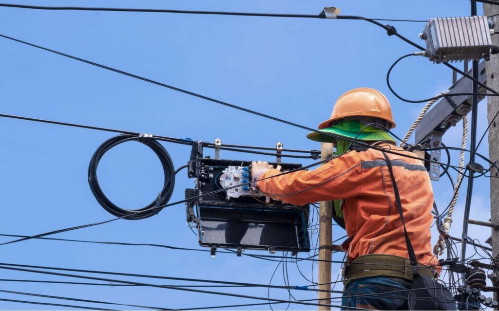 An electrician in safety gear working on a power line against a clear blue sky