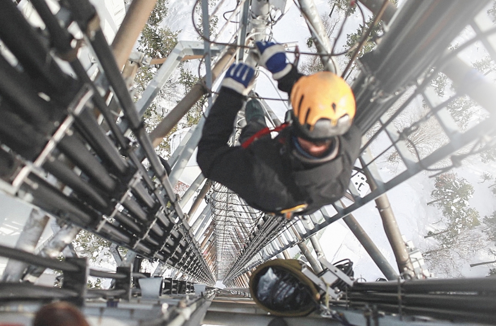 a tower technician in safety gear working high above the ground