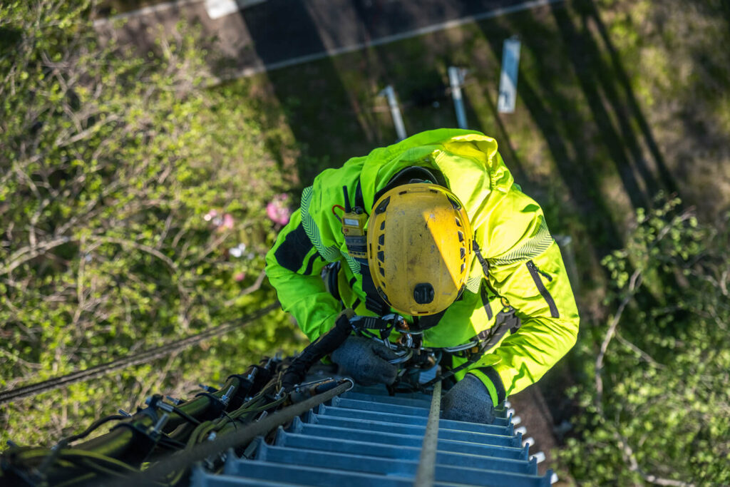 A tower worker in yellow safety gear climbing a ladder