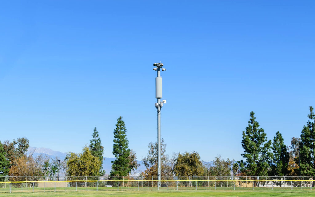 A small cell tower in a field with trees and mountains in the background