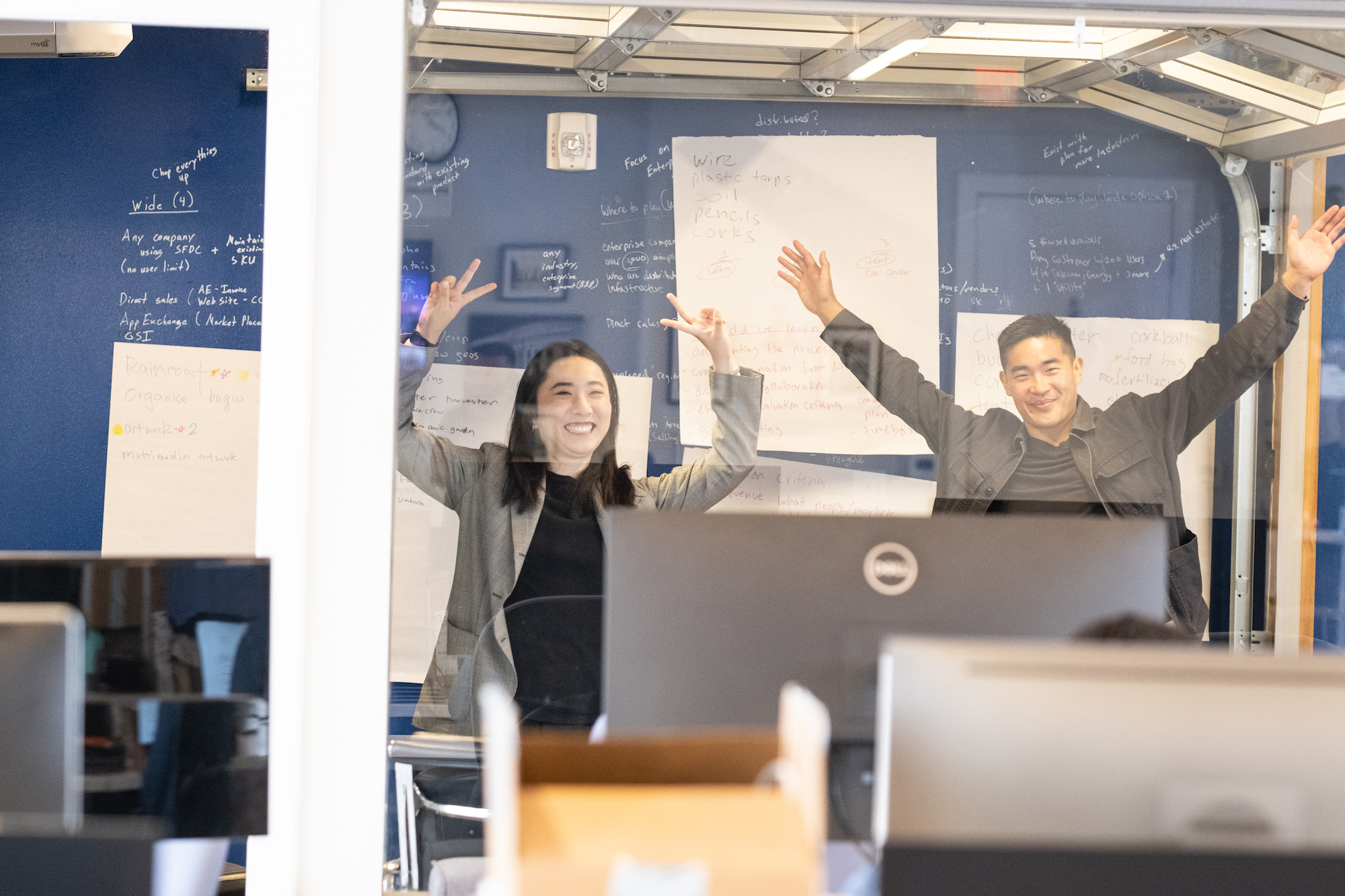 A male and female professional in an office with arms raised celebrating