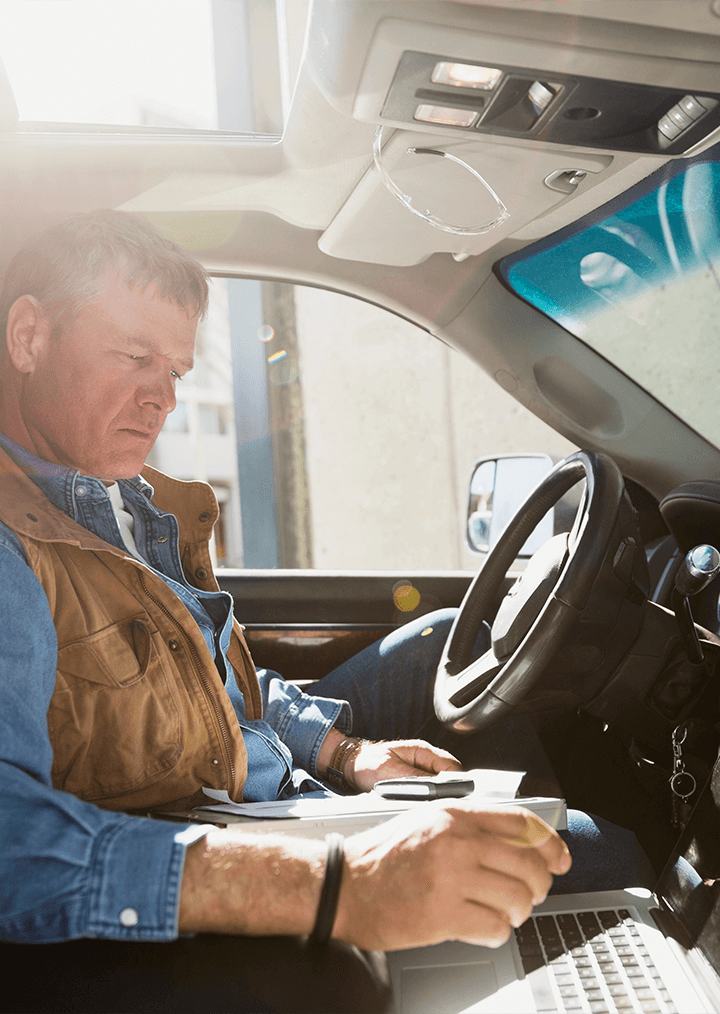 A man in a car types on a laptop