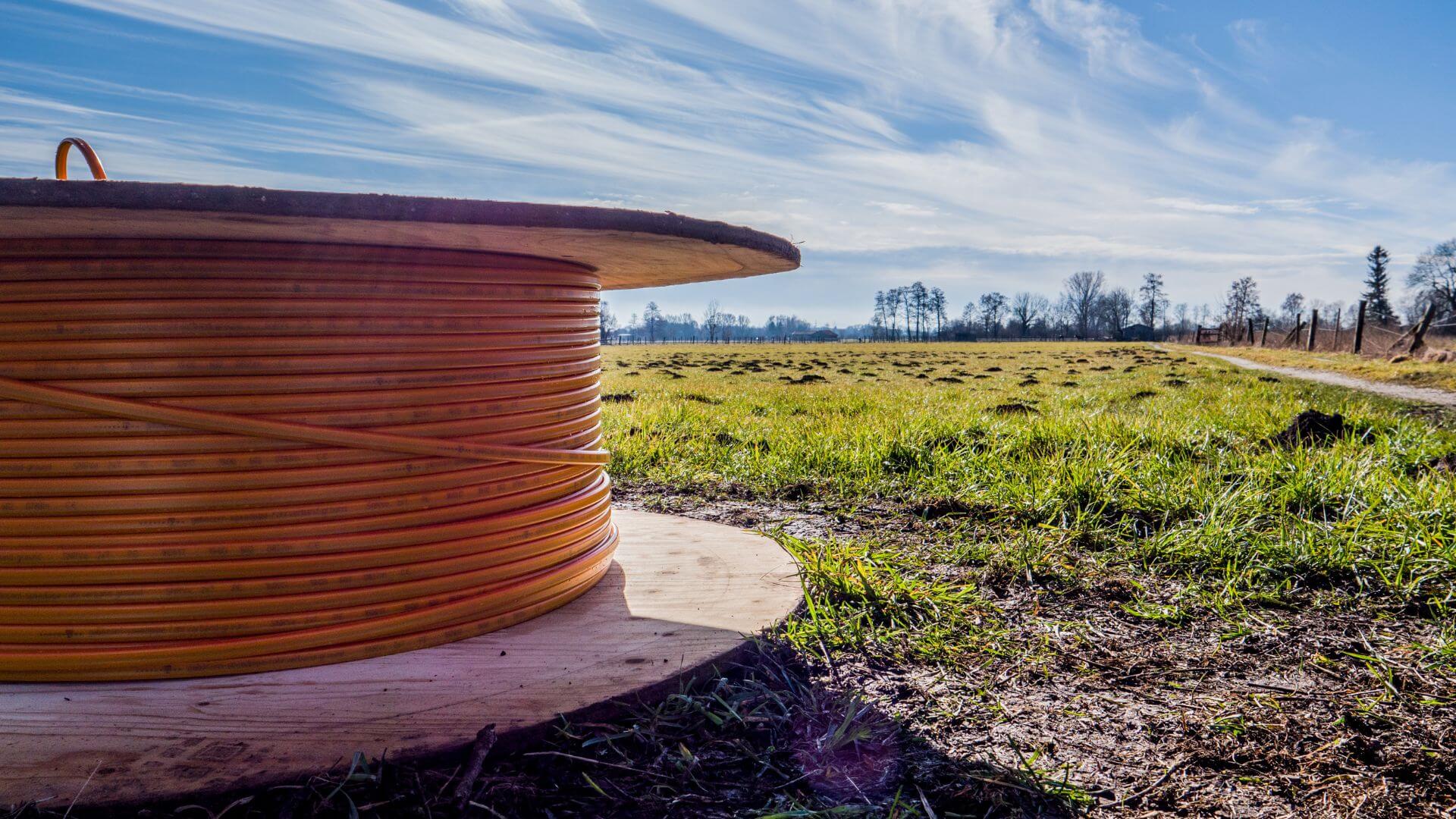 A large spool of orange fiber optic cables lays in a field of grass