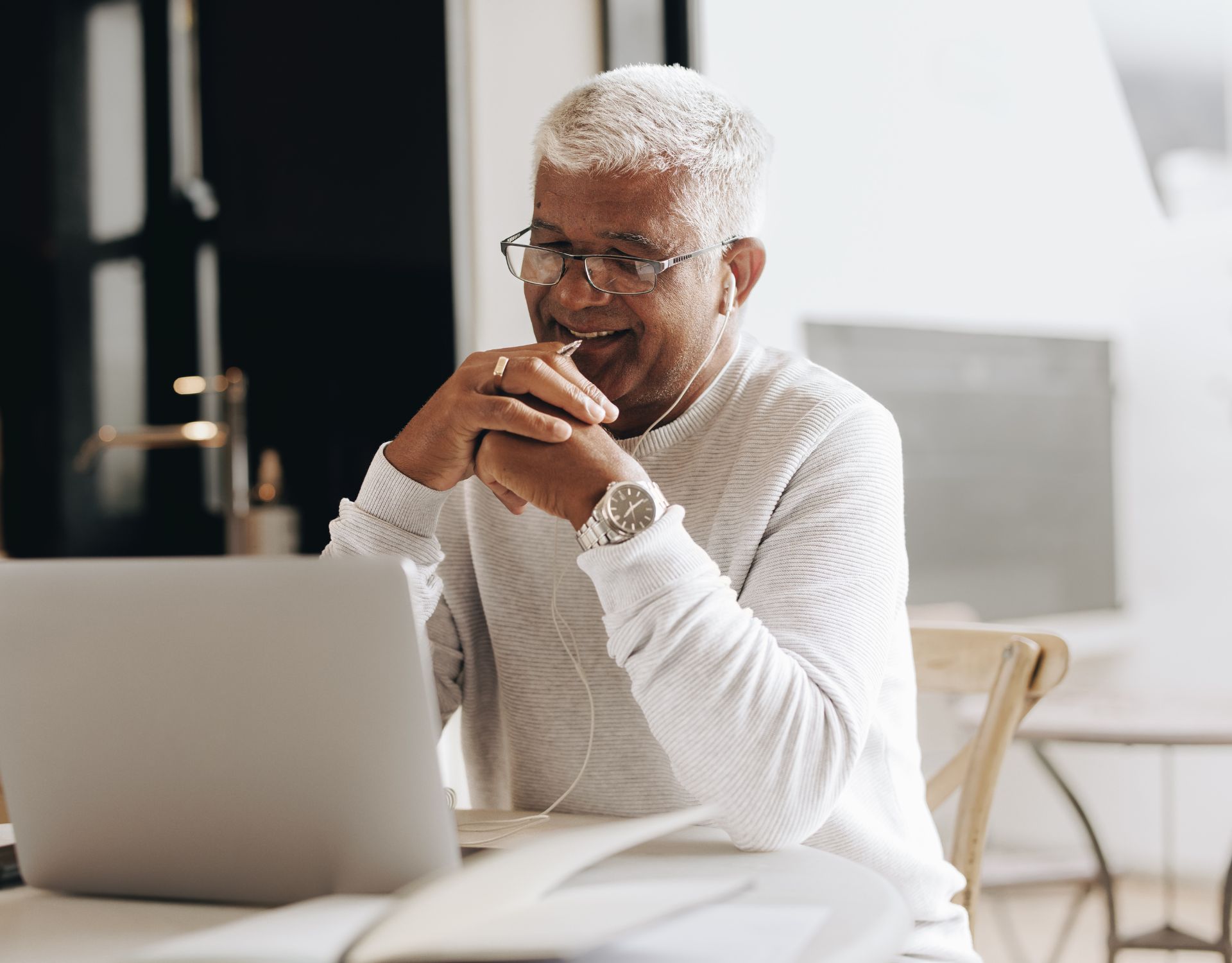 Man with glasses and a white turtleneck is sitting at a deck on his laptop