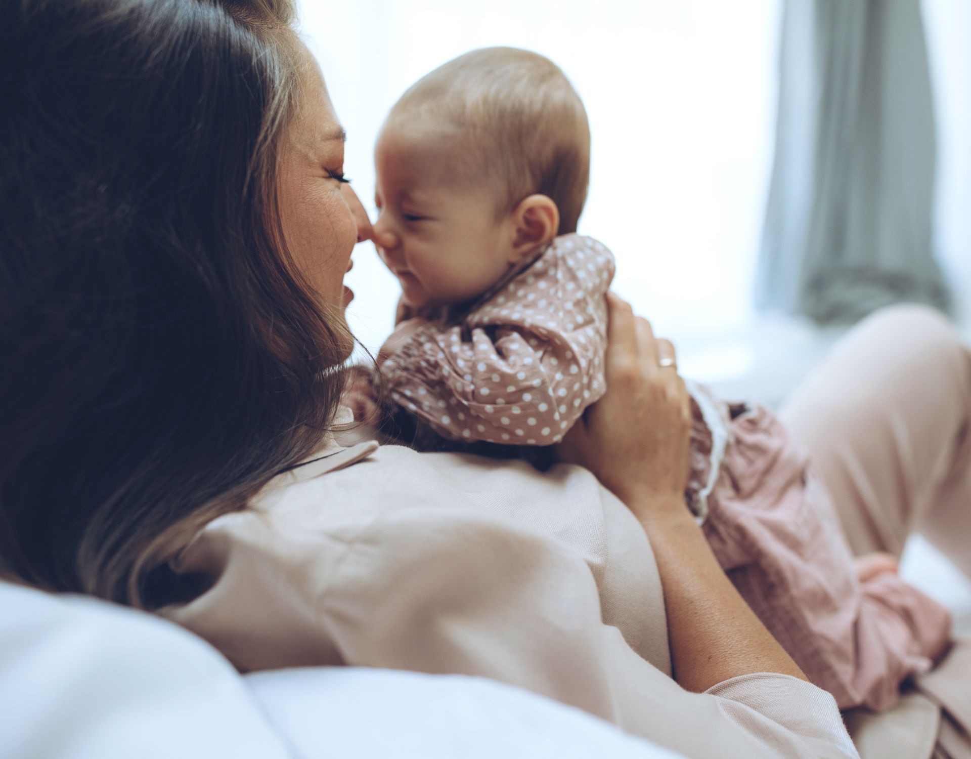 A woman holding her newborn baby as their noses touch