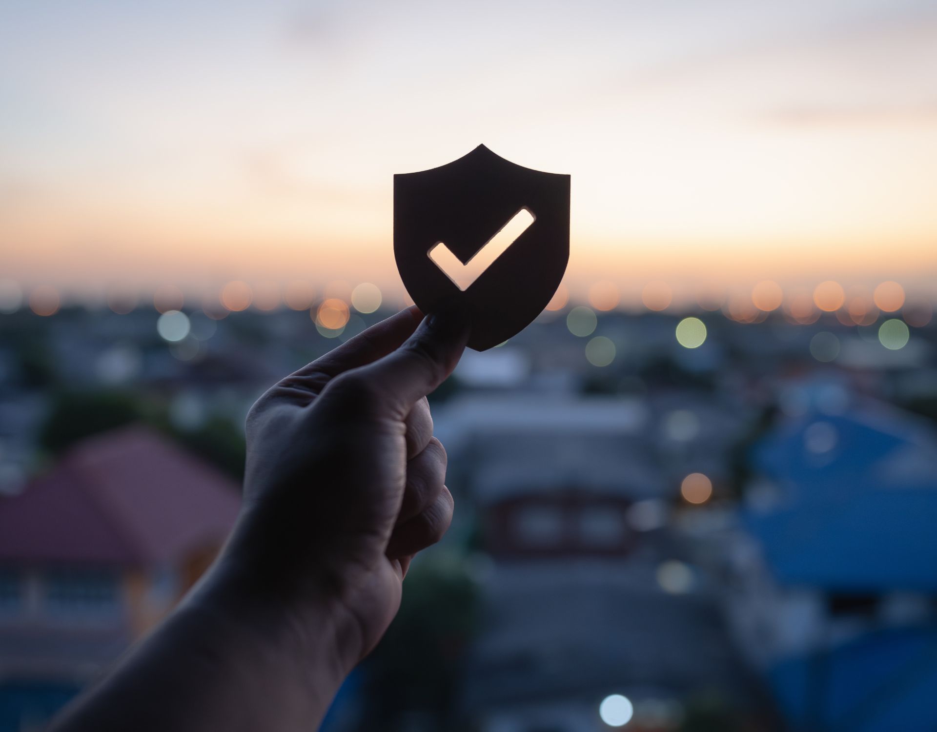A hand holding up a wooden security shield with a check mark cut out with a city background