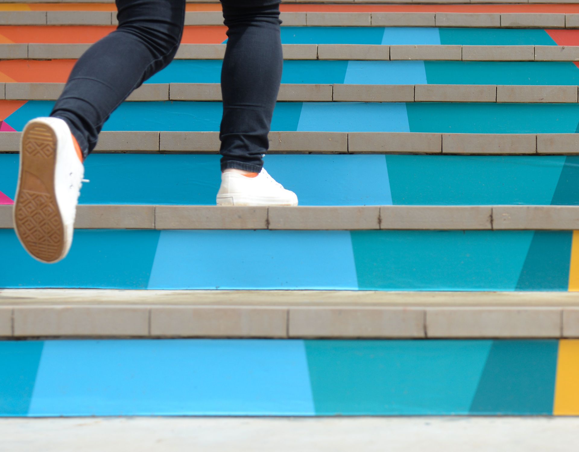 a close up of a man with white shoes walking up colorful stairs