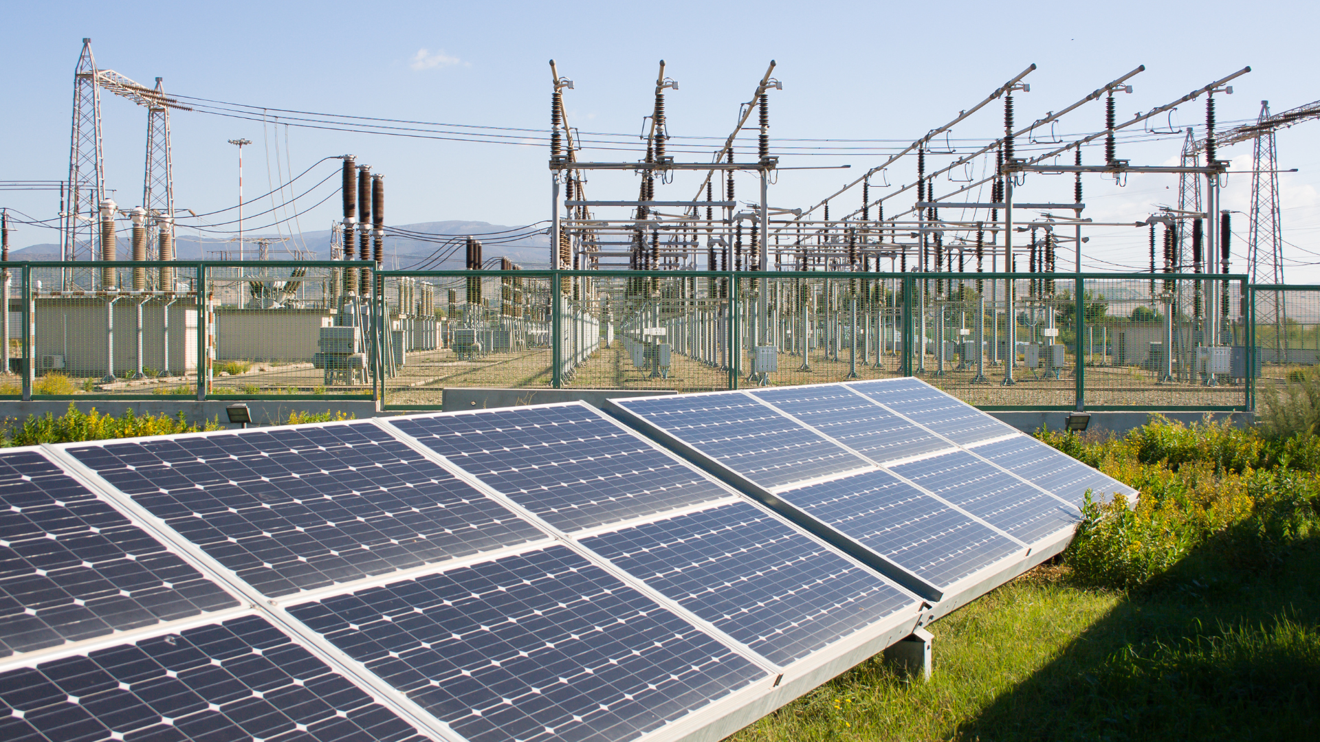 Solar panel array in the foreground with an electrical substation in the background