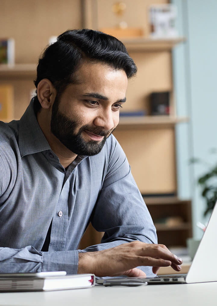 A young professional smiles softly while working on a laptop