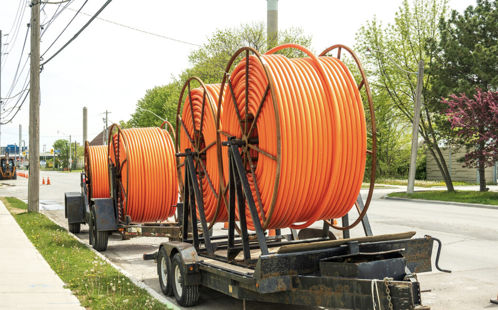 Large spools of orange cable loaded on a trailer parked on a roadside, likely for fiber network installation