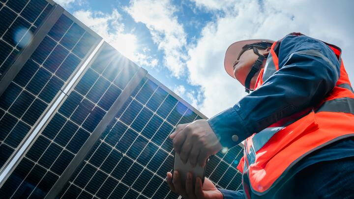 A field technician holding a cellphone and standing beside a solar panel