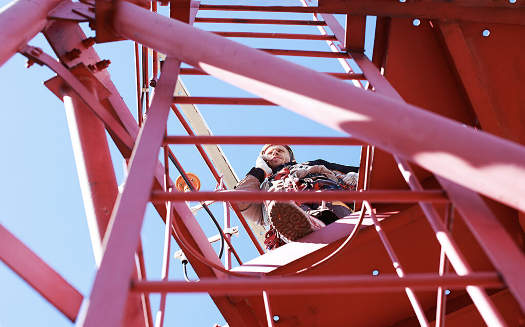 Close-up of a technician wearing safety gear while sitting on the red framework of a tower
