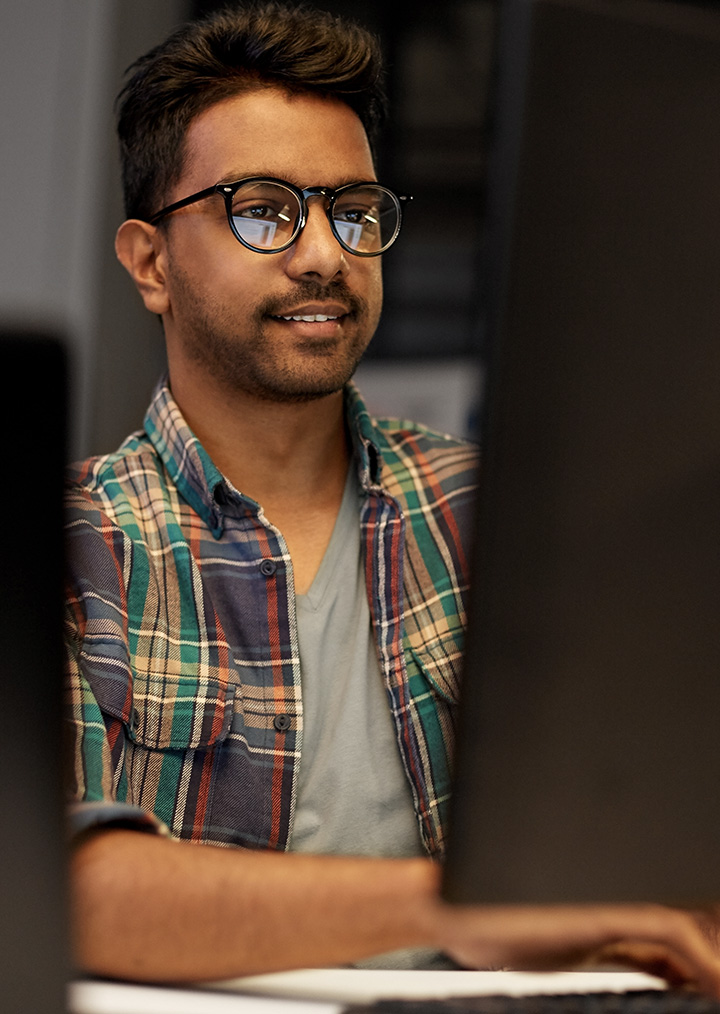 A smiling man with glasses looking at a computer monitor in an office setting
