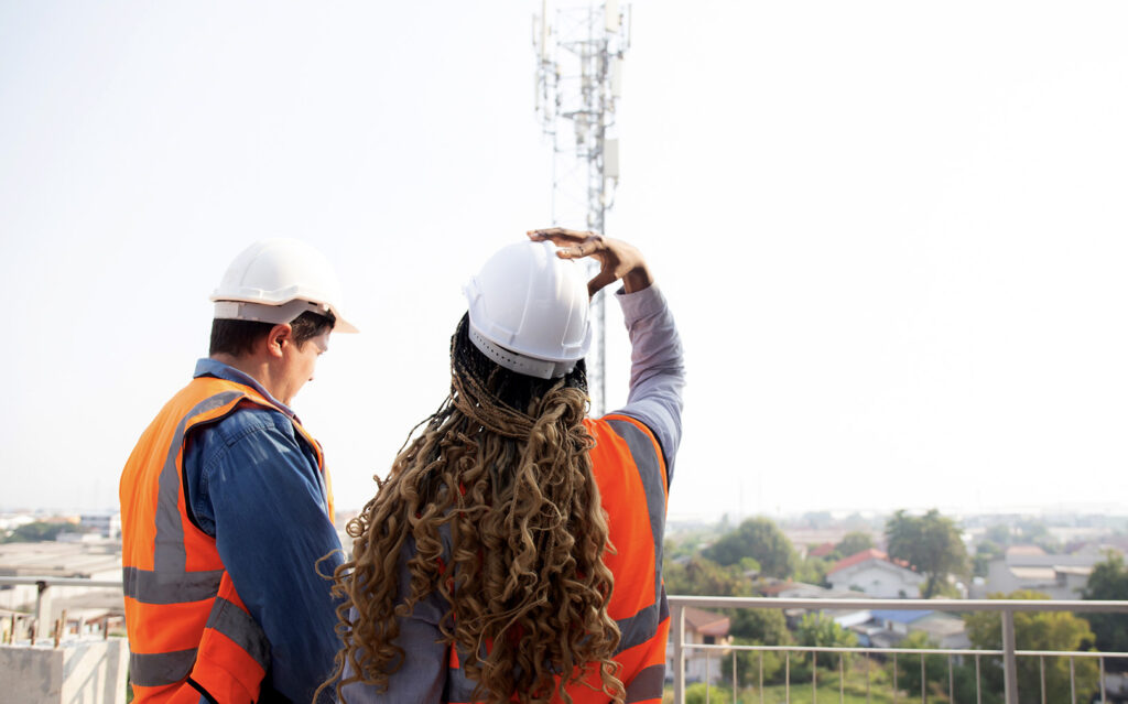 a man and woman in safety gear look at a wireless tower in the distance