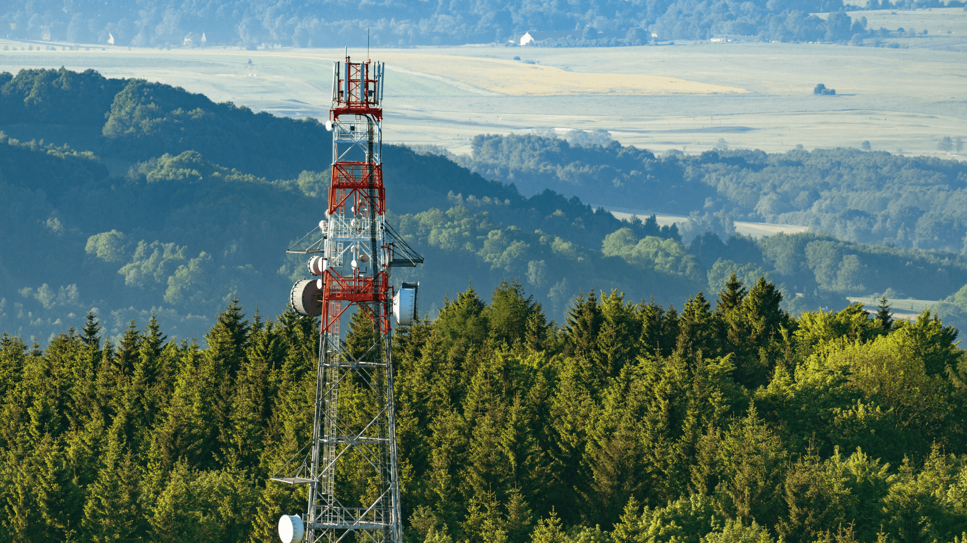 a telecommunication tower at the top of a wooded hill on an aerial shot