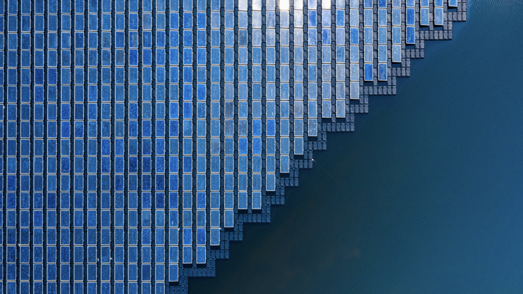 an aerial shot of a field of solar panels in a large body of water
