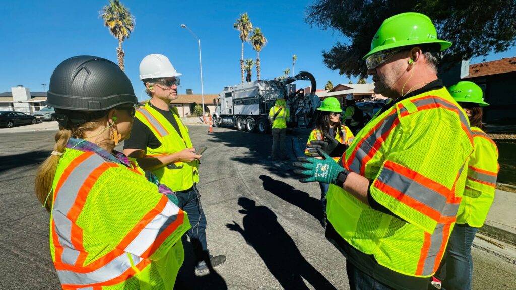 Team of workers in reflective safety vests and helmets having a discussion near a fiber deployment vehicle on a sunny residential street