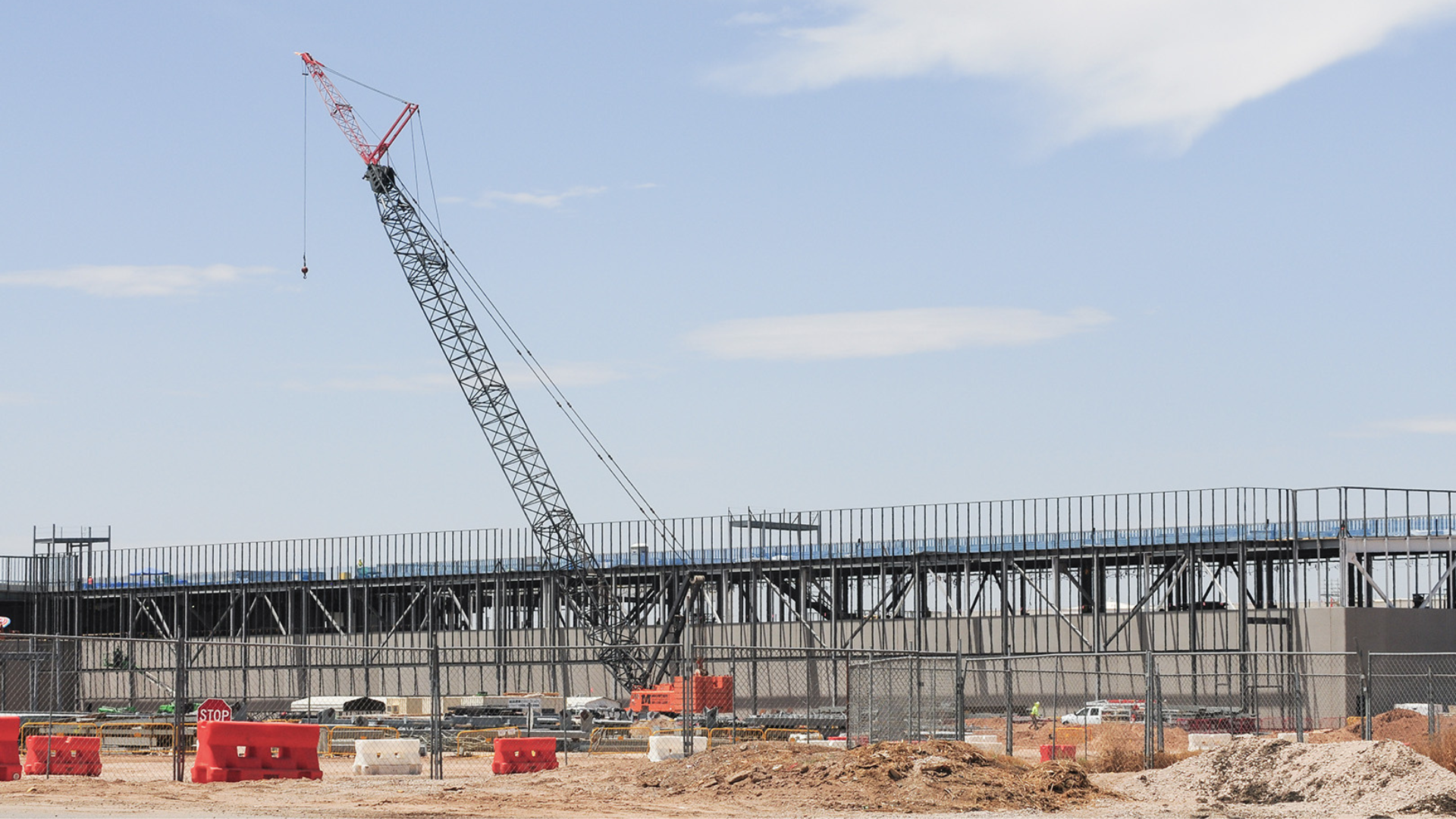 Construction site of a data center with a large crane lifting materials. The steel framework of the building is visible, with workers and vehicles operating in the background.