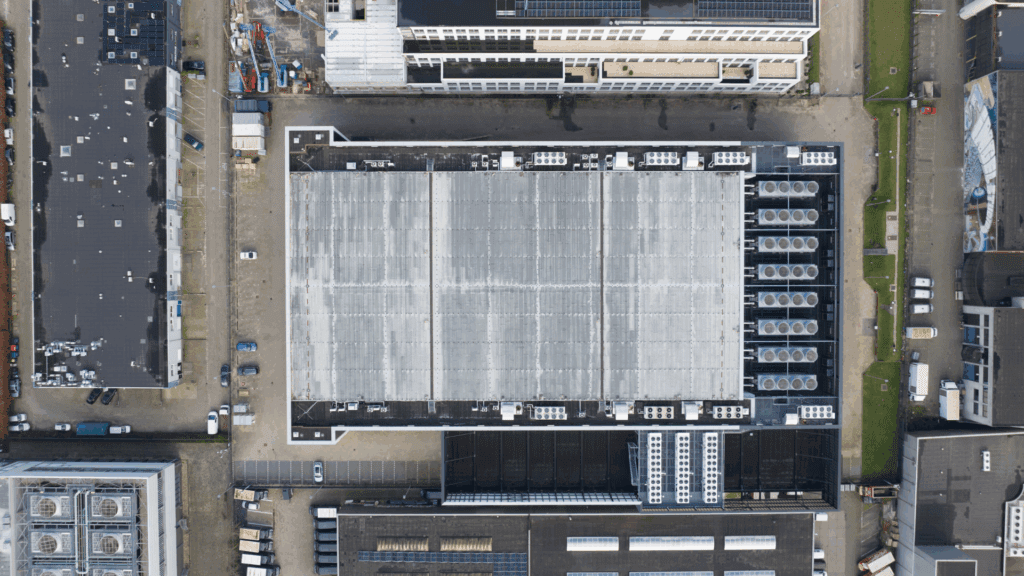 Top-down aerial view of a data center, with surrounding buildings, parking lots, and rooftop cooling systems.