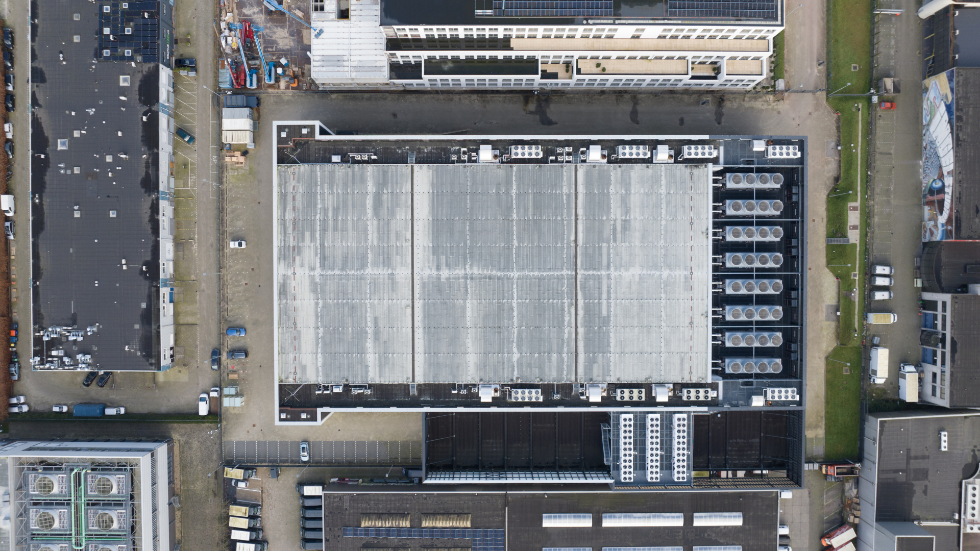 Top-down aerial view of a data center, with surrounding buildings, parking lots, and rooftop cooling systems.
