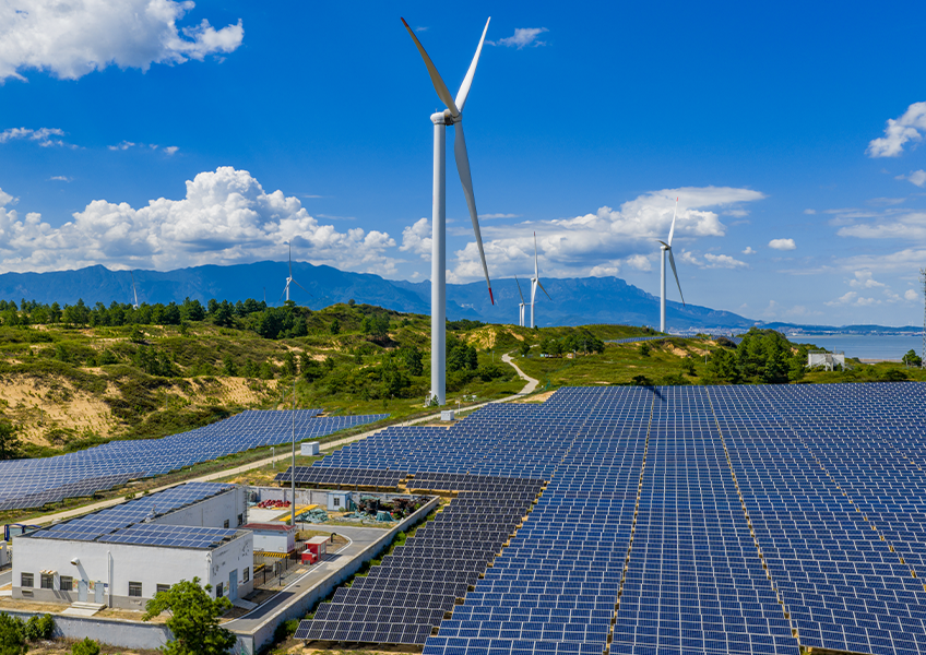a field of solar panels beside wind turbines and a power plant