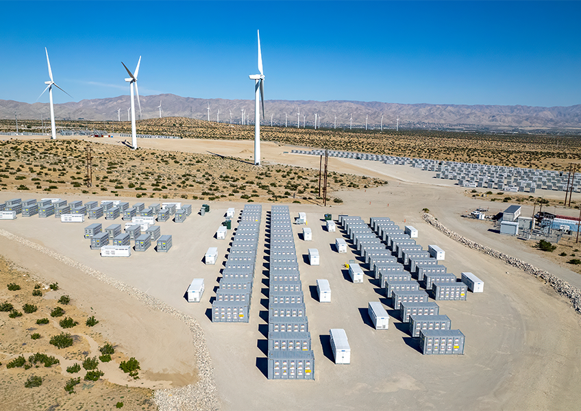 Battery energy storage system deployed in a desert landscape alongside wind turbines