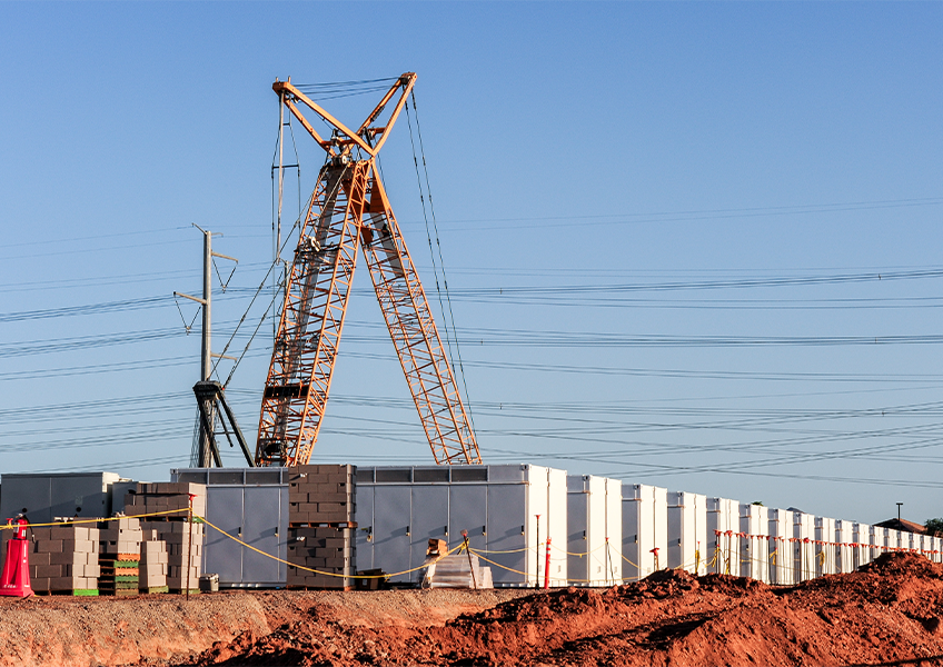 Battery energy storage system under construction with cranes, utility lines, and containerized battery units