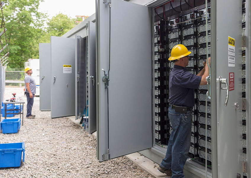 Technicians performing maintenance inside open battery energy storage system cabinets at an outdoor site