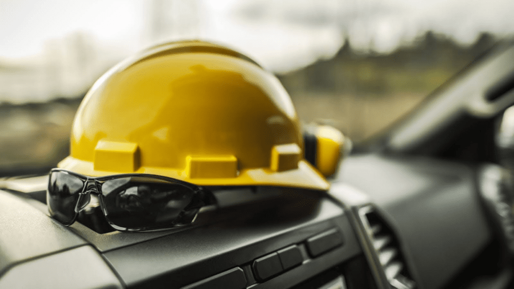 Yellow construction hard hat and black safety sunglasses resting on a vehicle dashboard